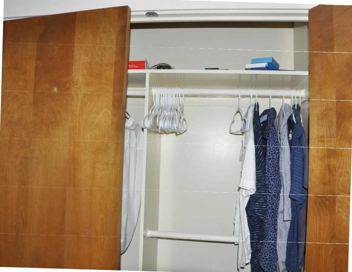 Open wooden closet doors revealing empty hangers, hanging shirts and boxes on an upper shelf.