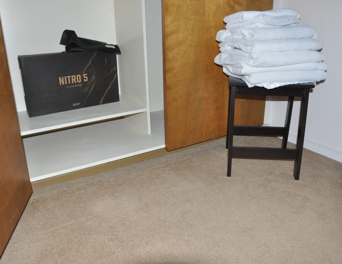 Closet bottom shelf with a Nitro 5 box; folded white towels sit on a black stool beside it.