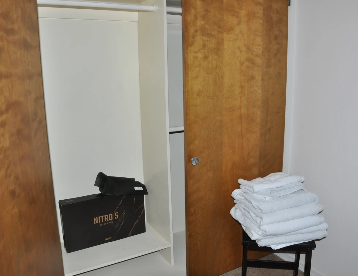 Open closet with a black box on its lower shelf and folded white towels on a stool.