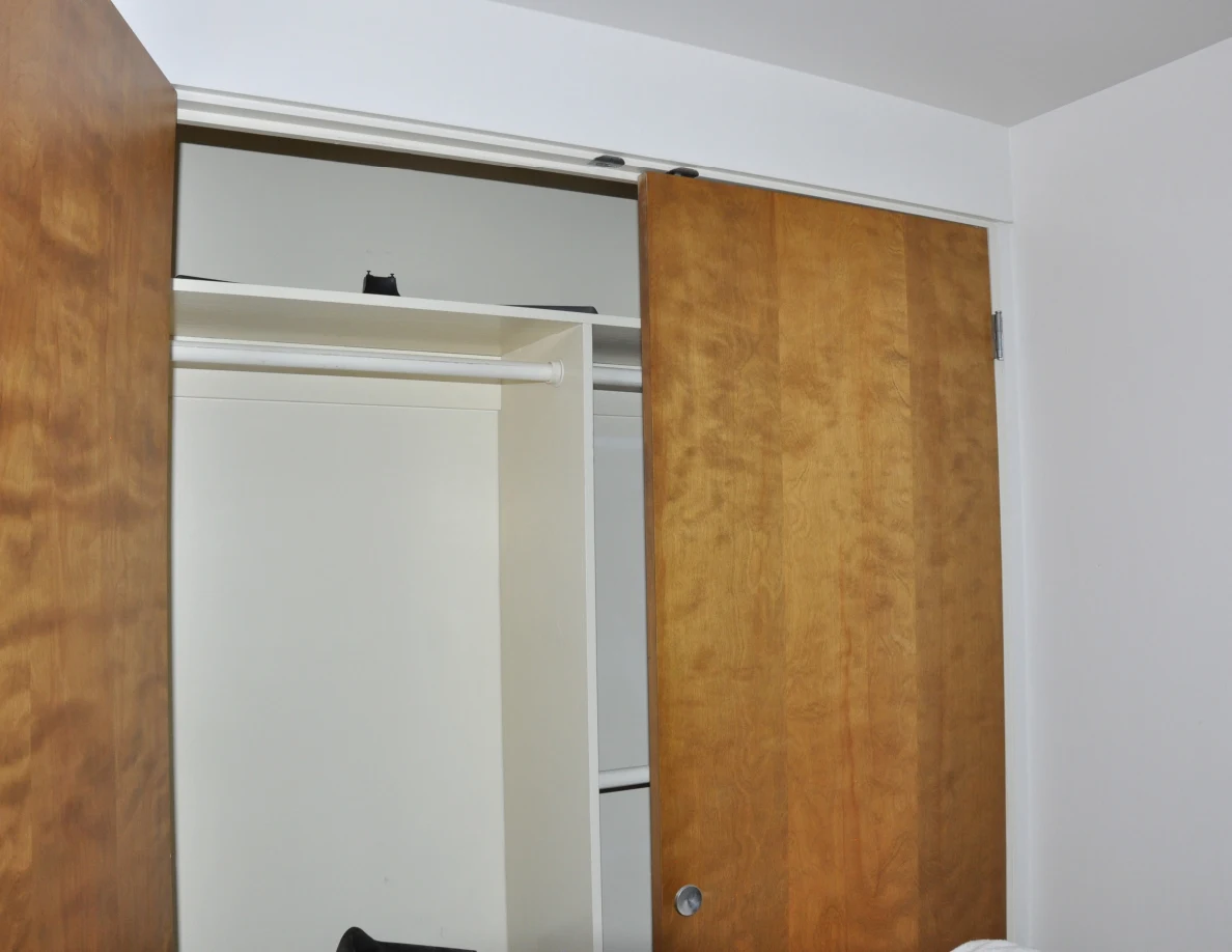 Mostly empty open closet with a rail, upper shelf and wooden sliding door.