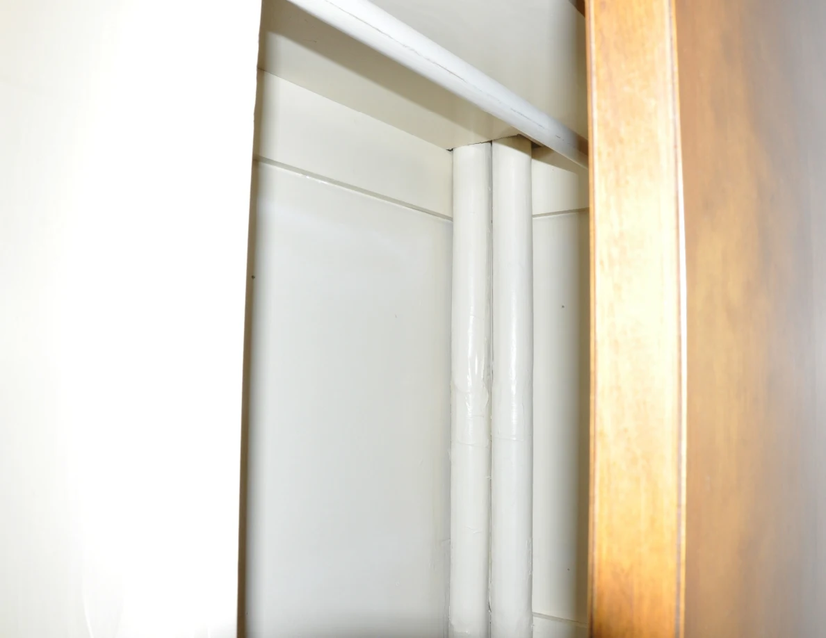 Close view of white pipes running vertically inside a closet beside a hanging rail.