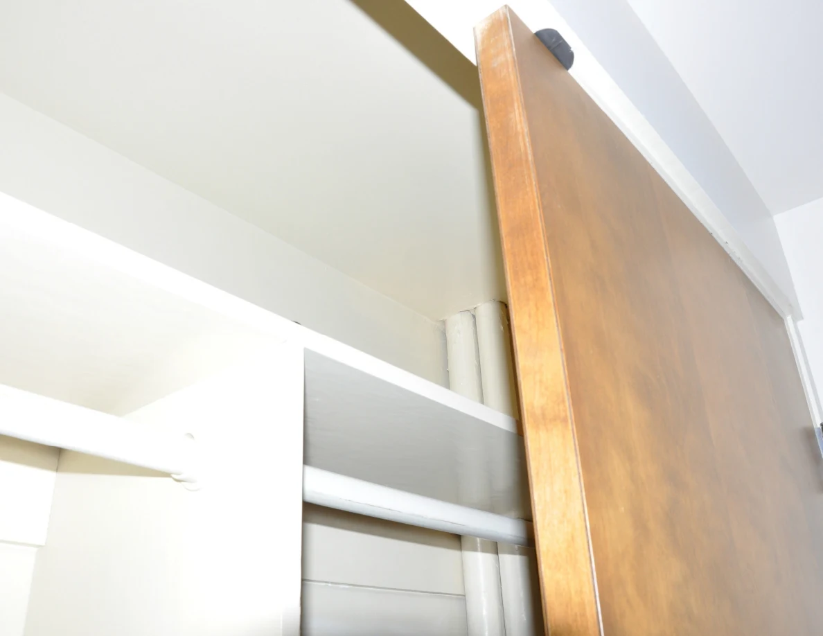 Upper closet shelving, rail and wooden door with a small dark fitting near its top.