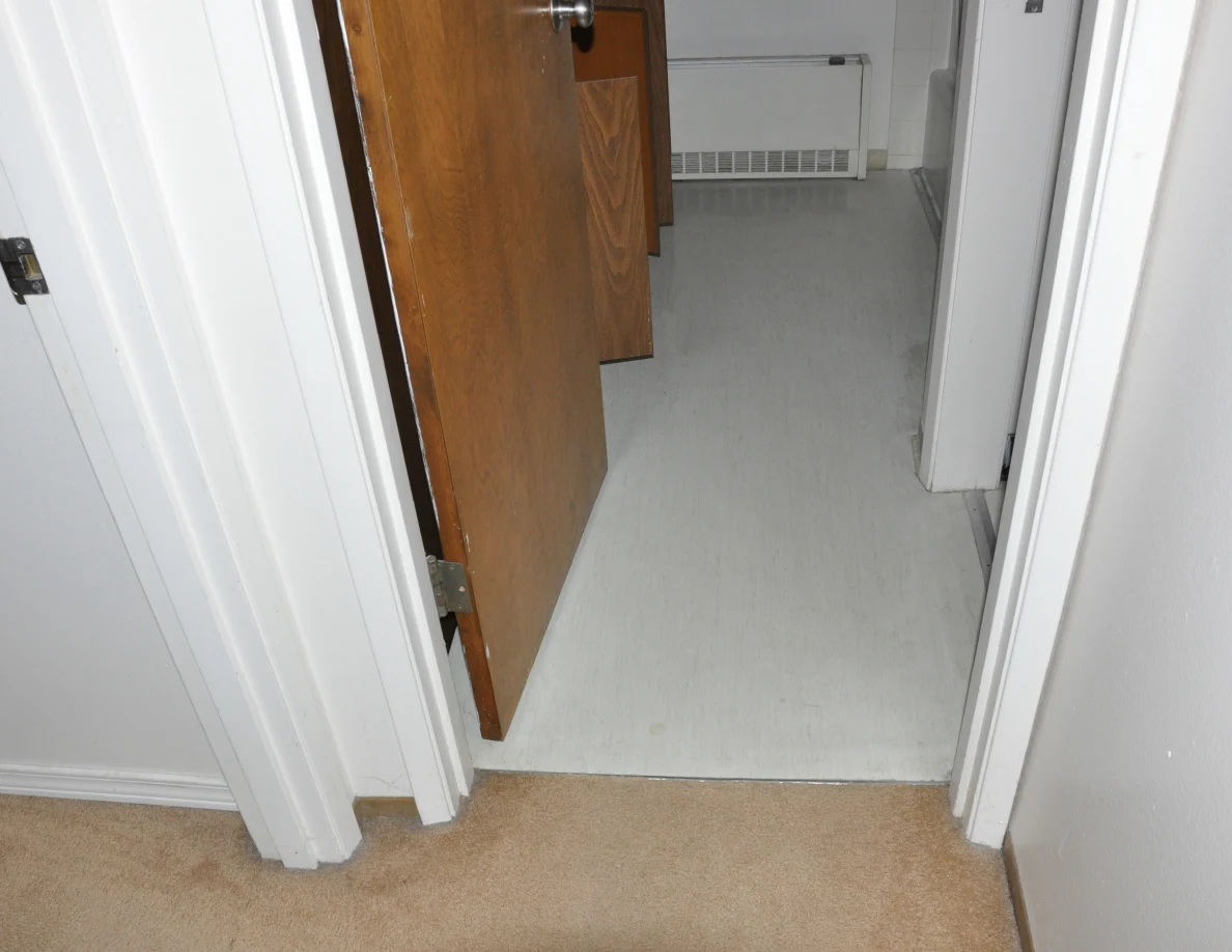 Open bathroom doorway showing pale flooring and a wall heater beyond.