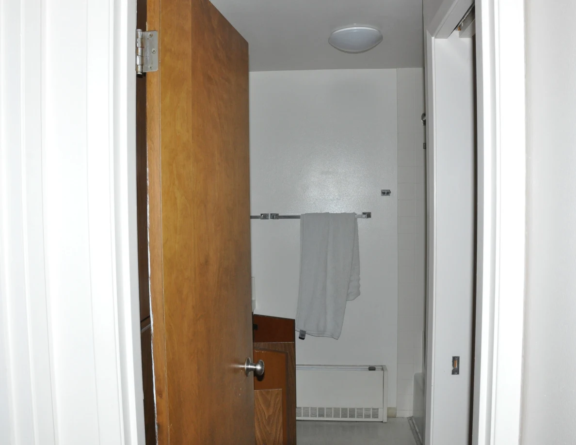 Bathroom doorway with an open wooden door, gray towel, wall heater and ceiling light.