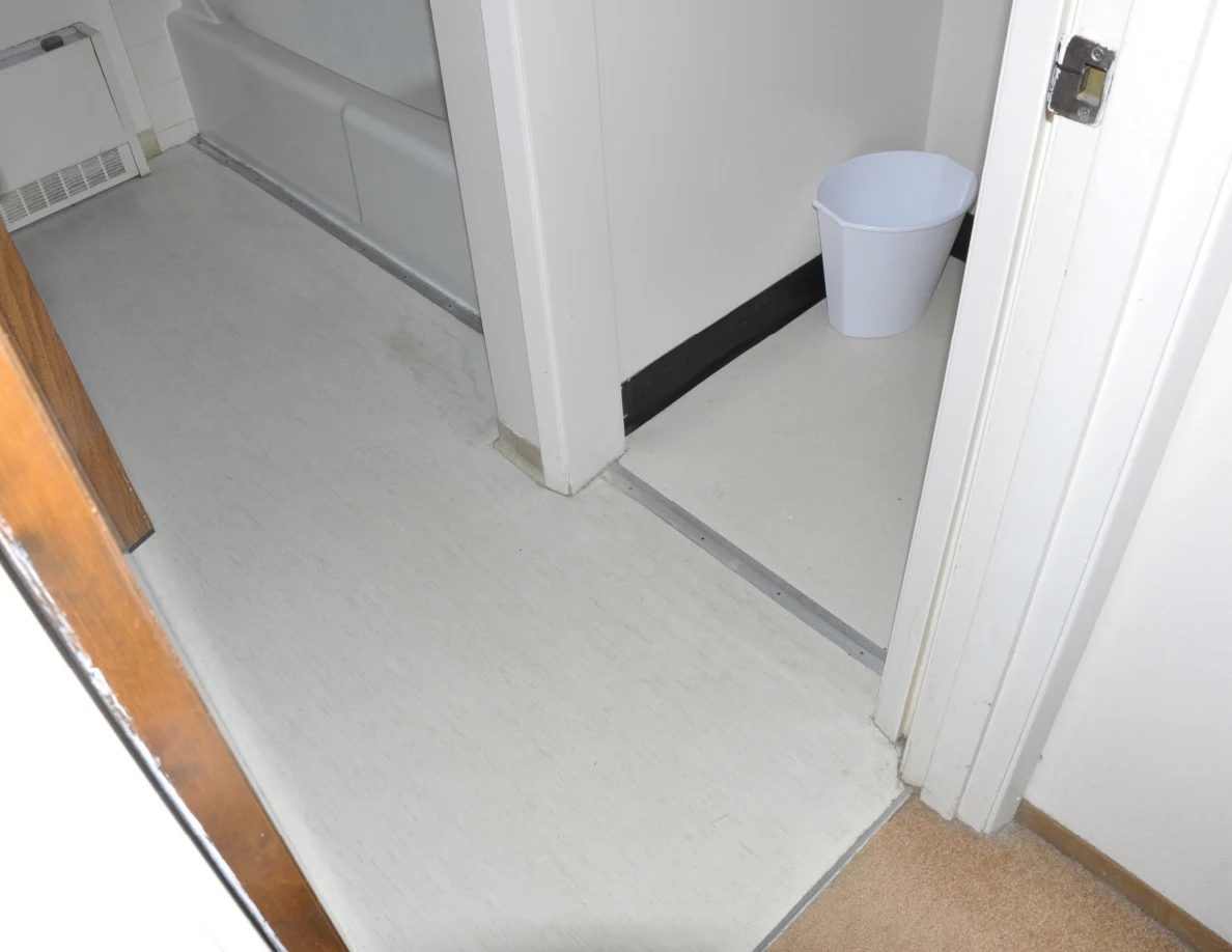 Bathroom floor at a doorway with a bathtub edge and white wastebasket.