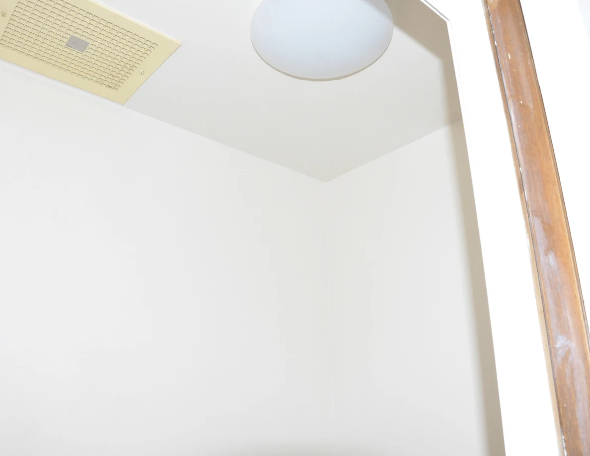 Toilet compartment ceiling with a rectangular vent and round light fixture.