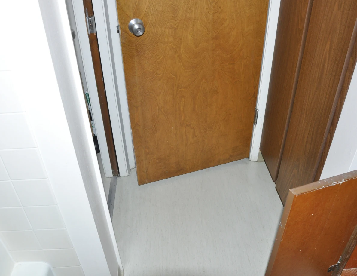 Bathroom floor and open wooden door beside a tall wooden cabinet.