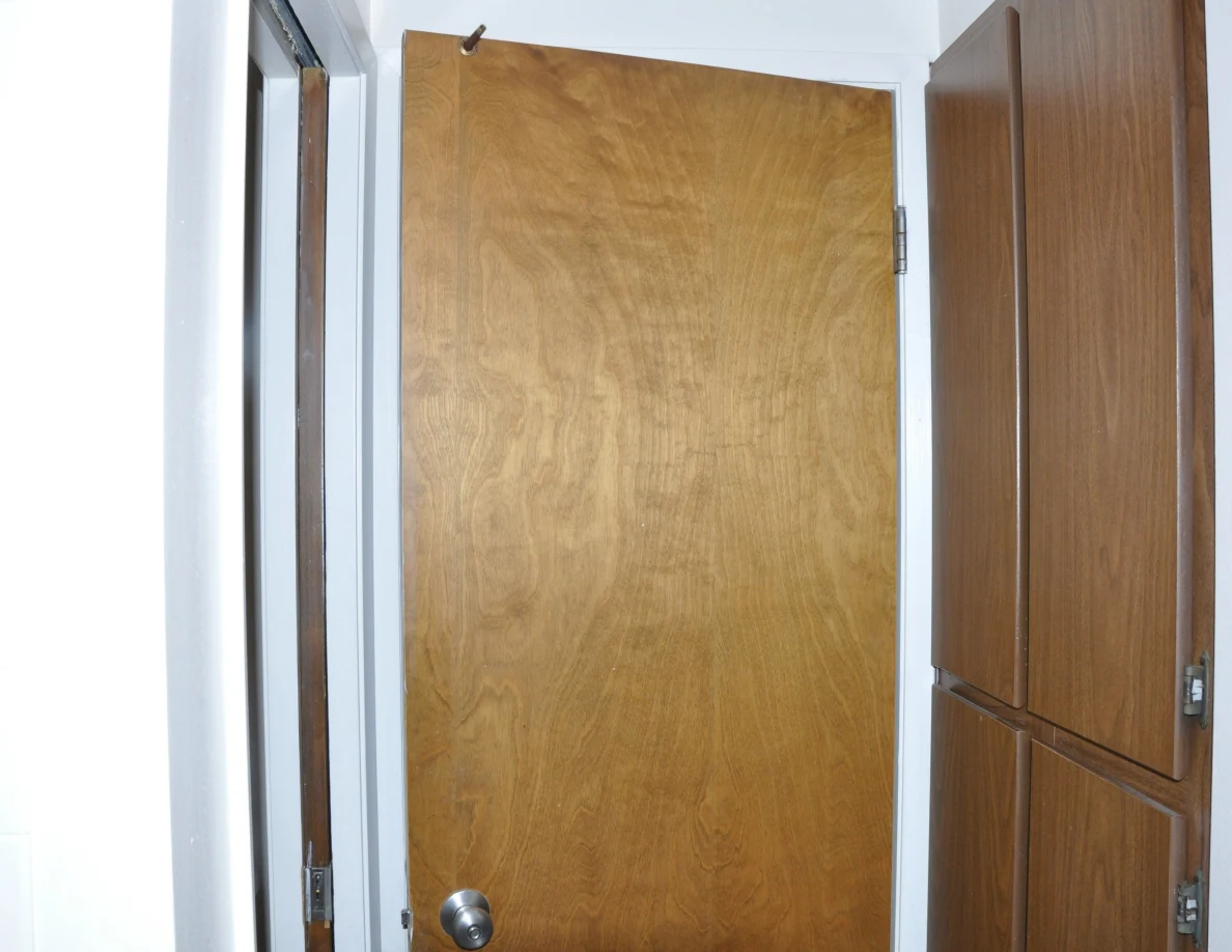 Open wooden bathroom door beside a tall wooden storage cabinet.