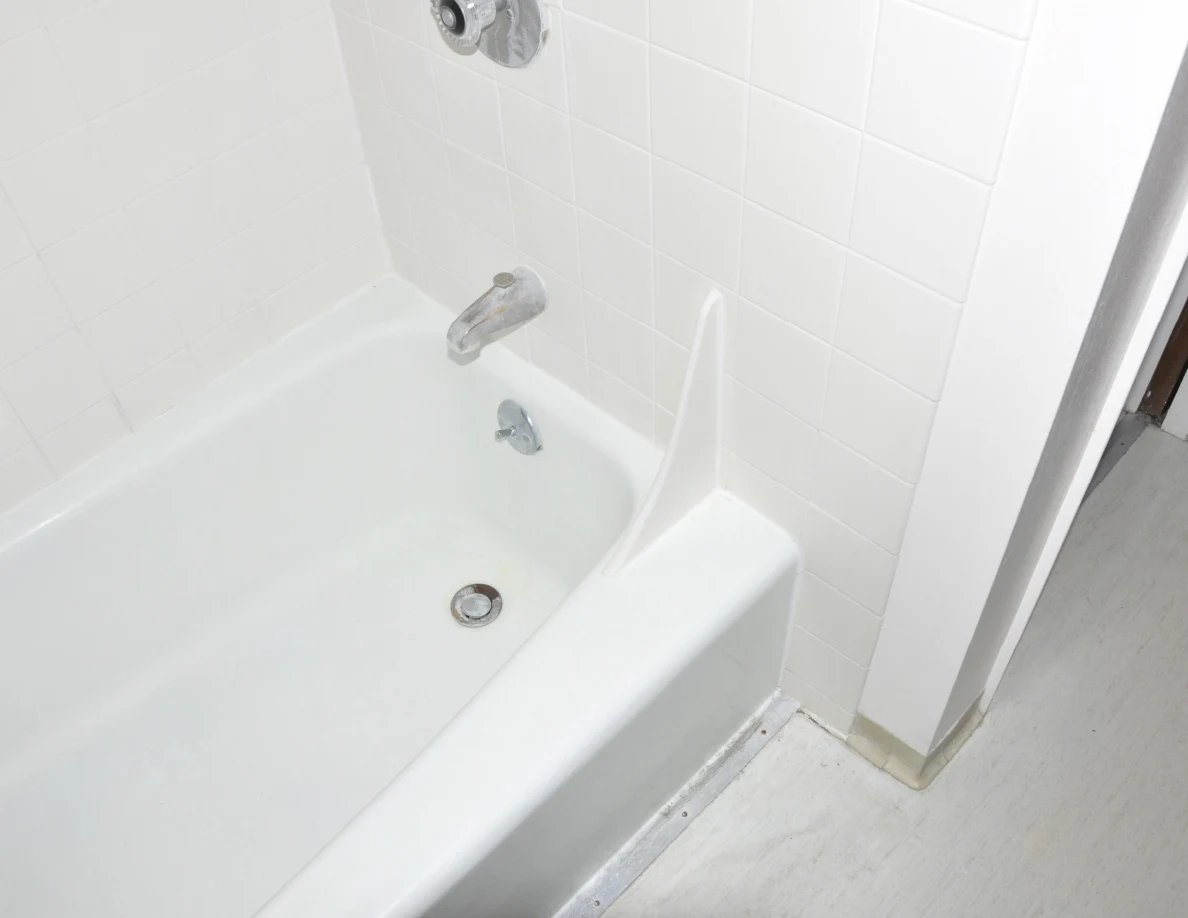 White bathtub corner with chrome spout, drain and tiled walls.