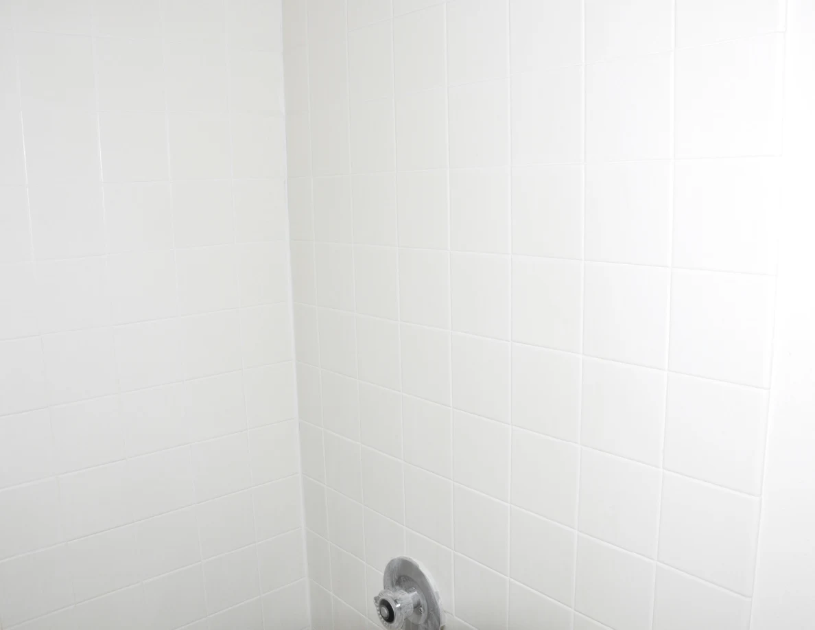 White tiled shower walls with part of a chrome control visible.