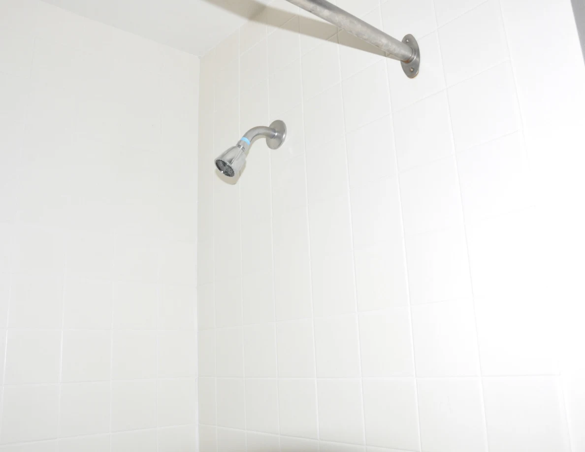 Chrome showerhead and curtain rail against white tiled walls.