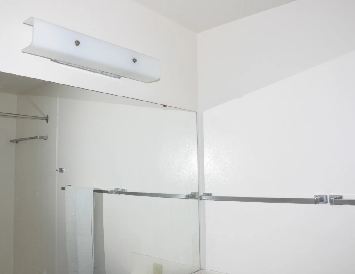 Bathroom mirror and rectangular wall light above empty metal towel bars.