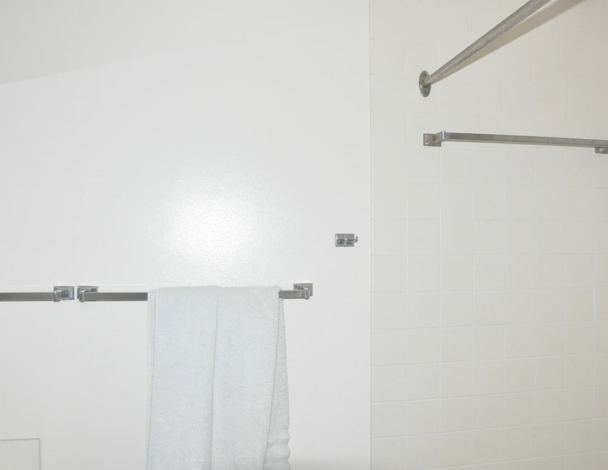Bathroom wall with a gray towel, tiled shower surround and metal curtain rail.