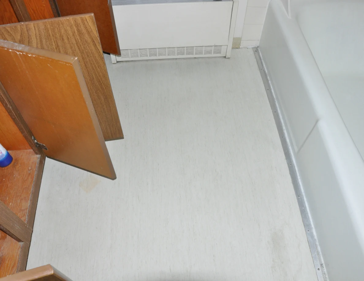 Pale bathroom floor between open vanity doors and the bathtub.