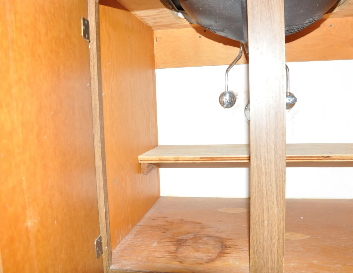 Open sink cupboard showing the basin underside, valves and a circular mark on its floor.
