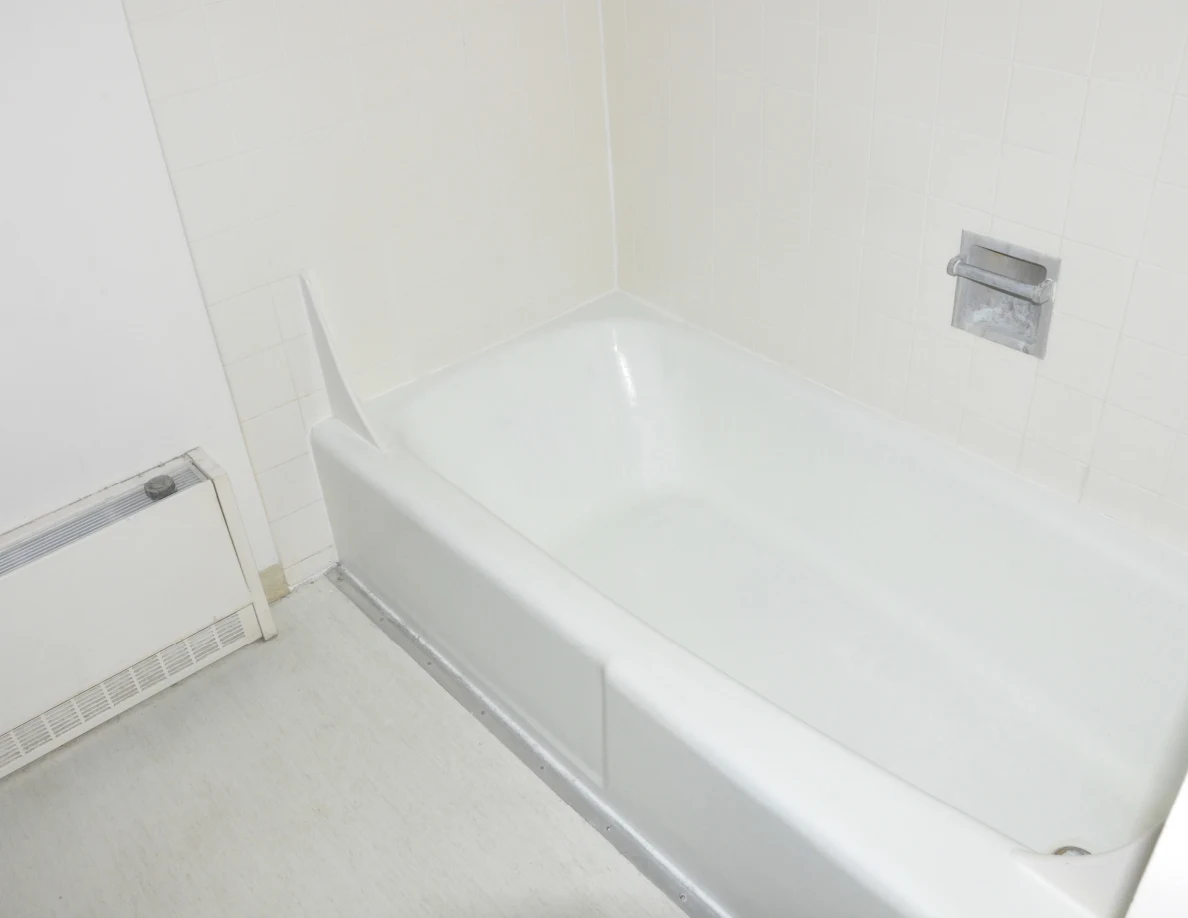 White bathtub beside a wall heater, with a recessed soap holder in the tiled wall.