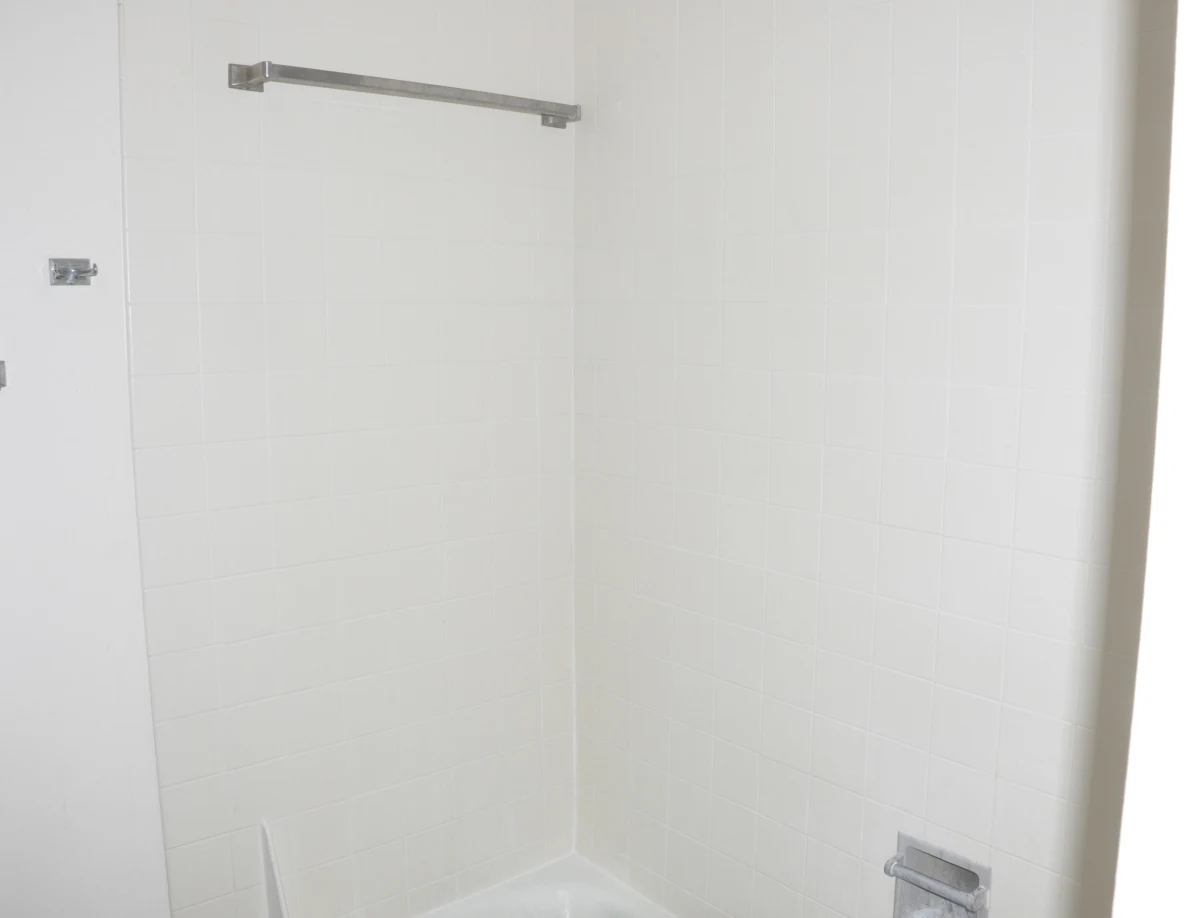 Tiled bathtub surround with a metal bar and recessed soap holder.
