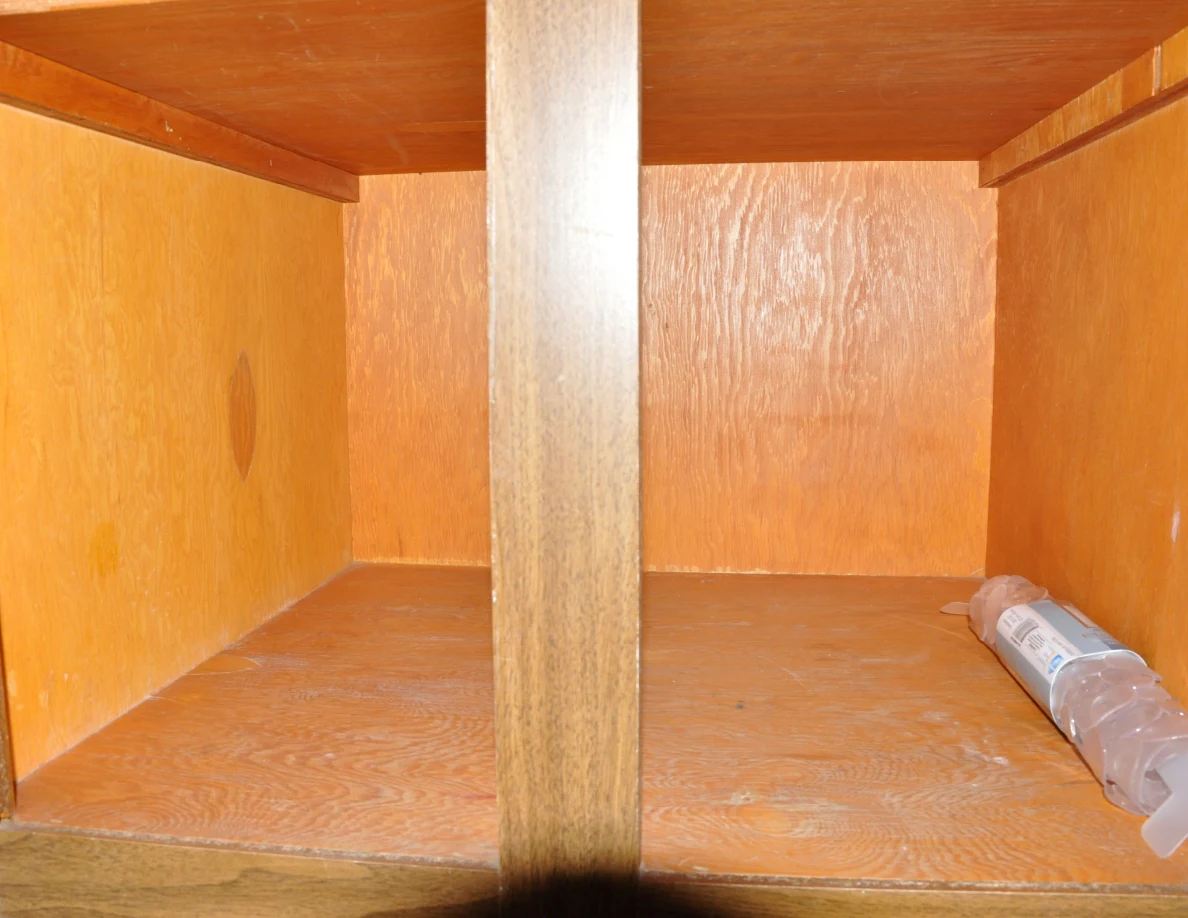 Open wooden cupboard containing a partly crushed plastic bottle.
