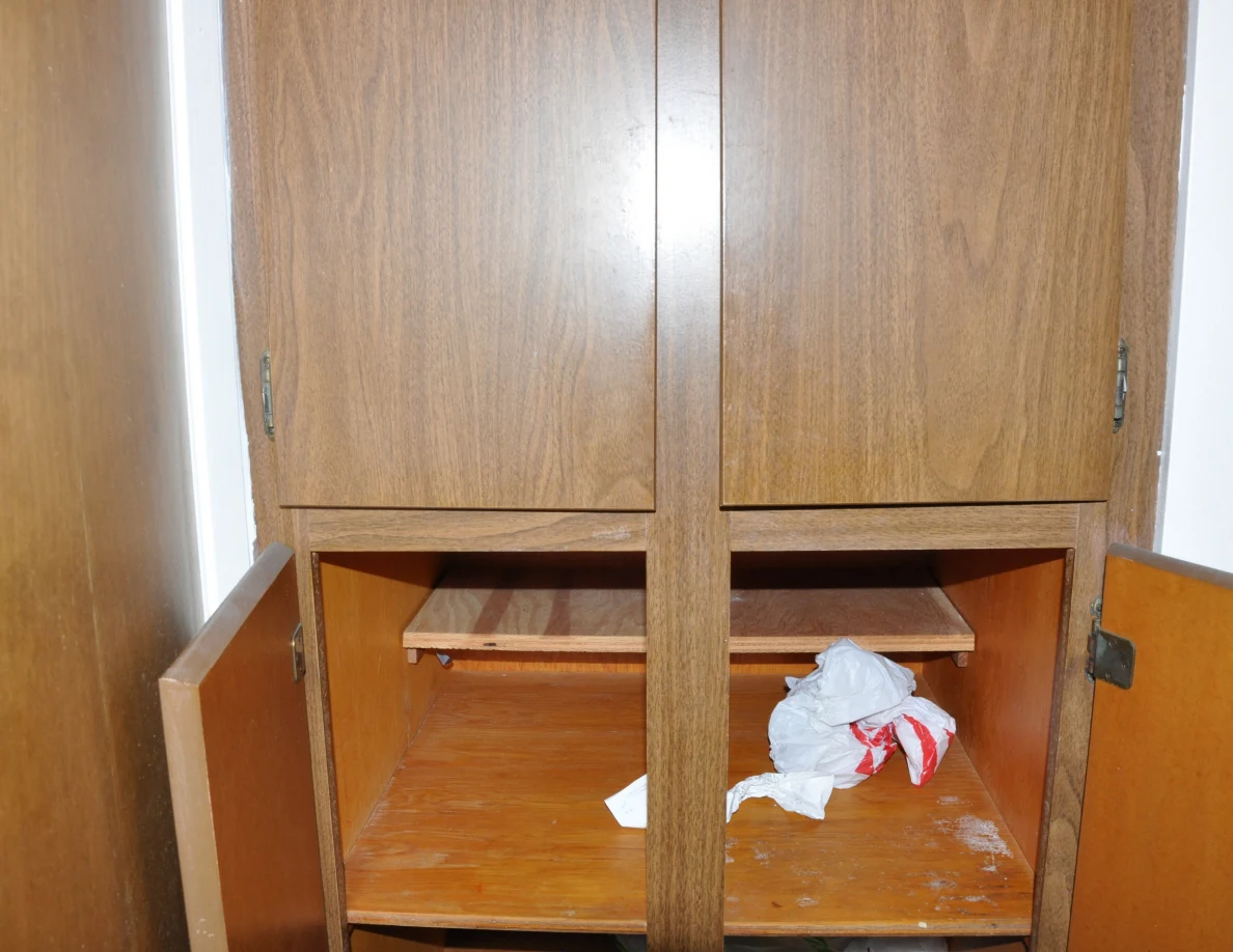 Wooden cabinet with closed upper doors and open lower shelves containing a crumpled bag.
