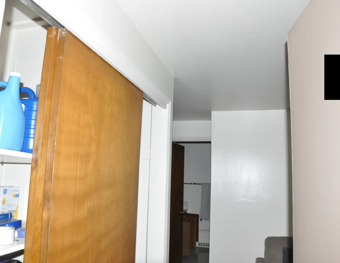 Upper doorway and wooden storage cupboard with large blue bottles on a shelf.