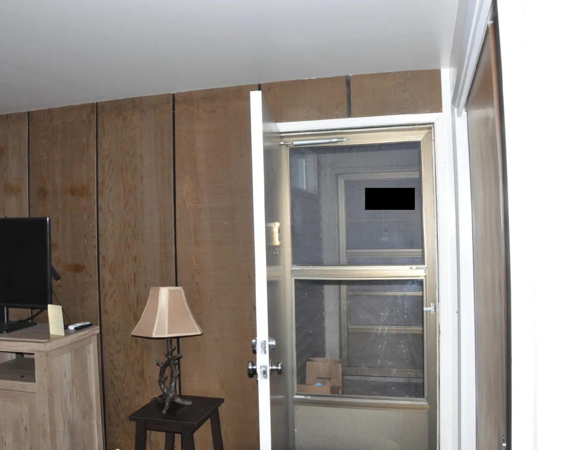Wood-paneled room with television, small lamp and an open entrance door with a black redaction.
