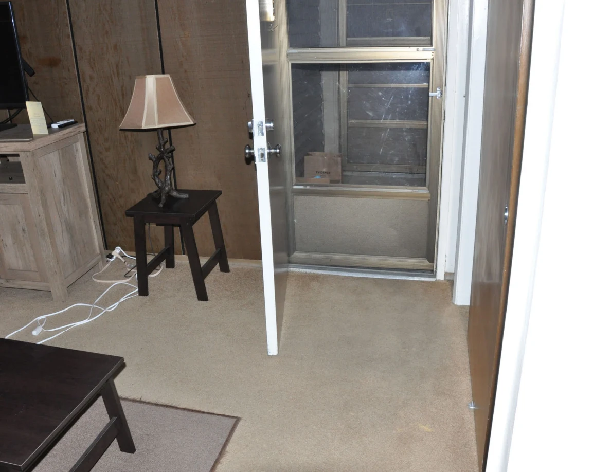 Carpeted entrance area with an open door, lamp on a stool and white cords on the floor.