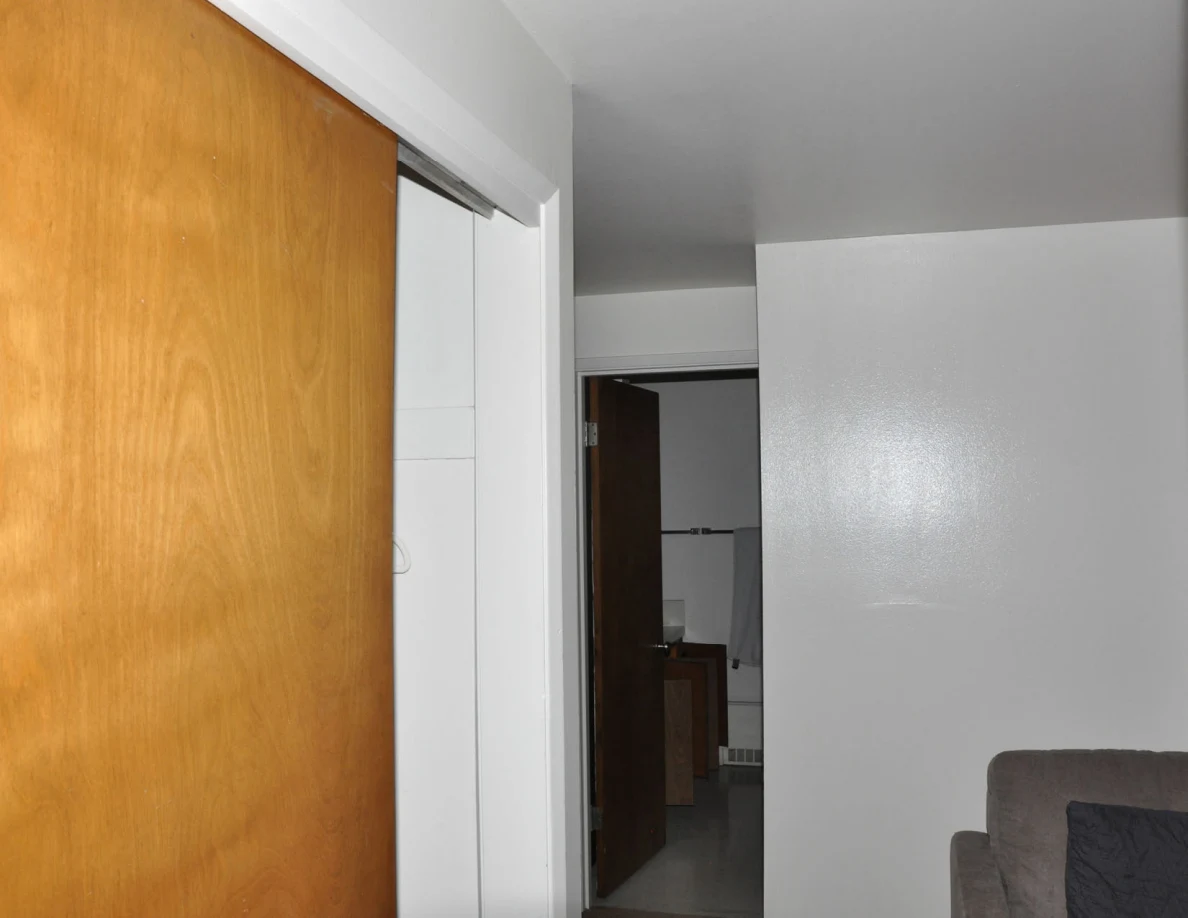 Wooden sliding closet door beside a hallway and the edge of a gray sofa.