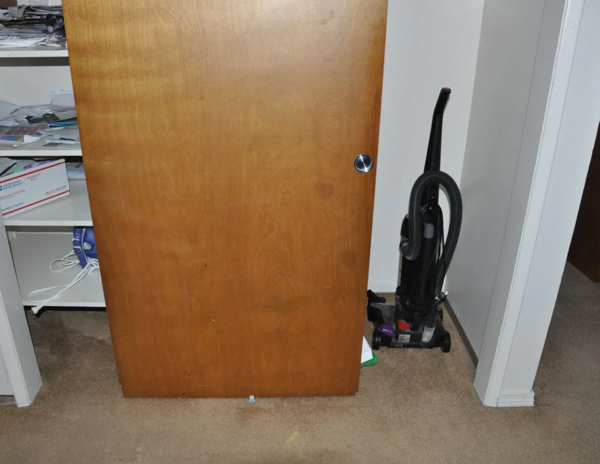 Upright vacuum cleaner beside a sliding wooden closet door and shelves of papers.