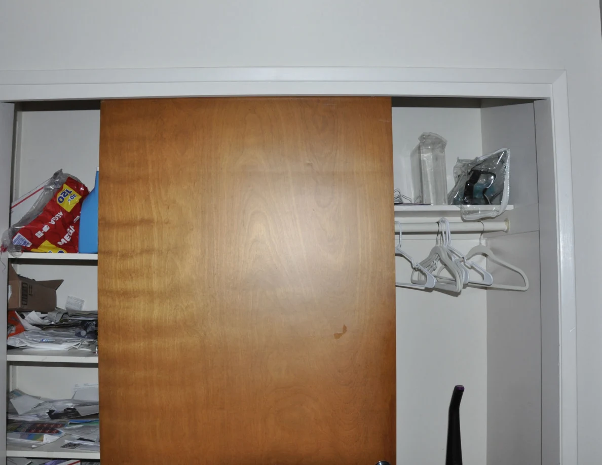 Storage closet with hanging clothes hangers, shelf contents and an upright vacuum.