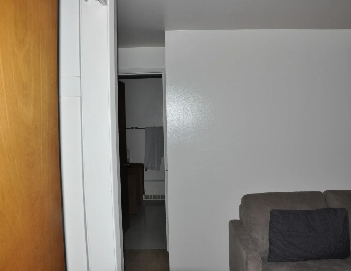 Living room wall and gray sofa beside a hallway and wooden closet door.