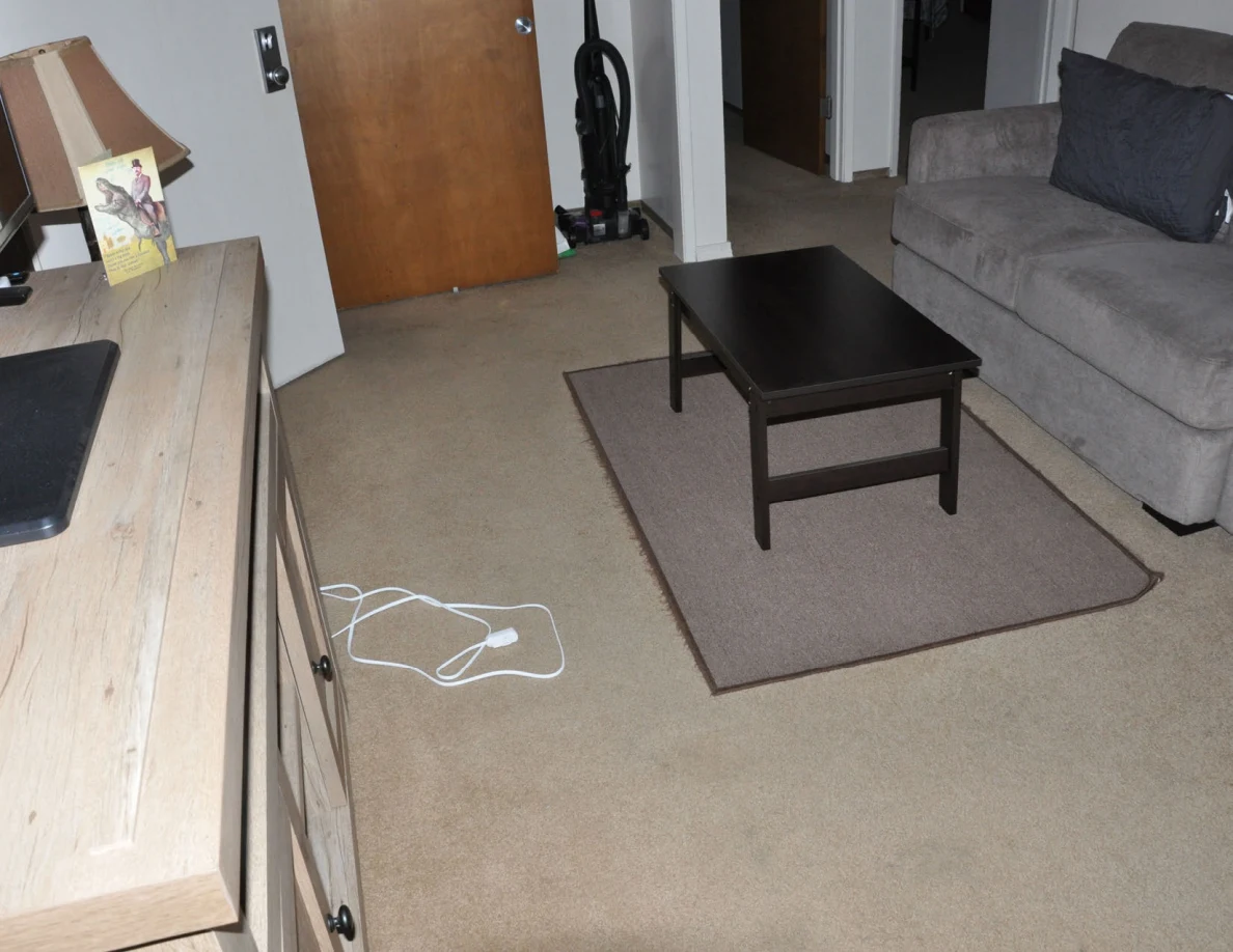 Dark coffee table on a rug between a gray sofa and television cabinet, with white cords nearby.