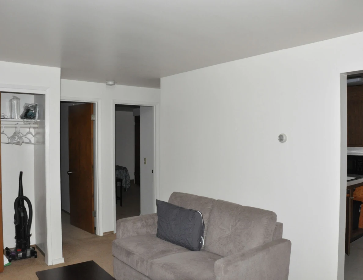 Gray loveseat, open closet and two interior doorways under a pale ceiling.