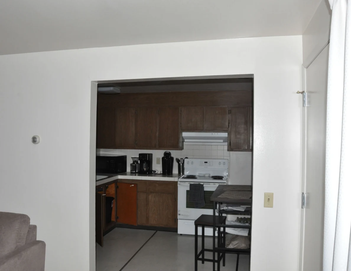 Kitchen entrance showing a white stove, wooden cabinets and a tall table with stools.