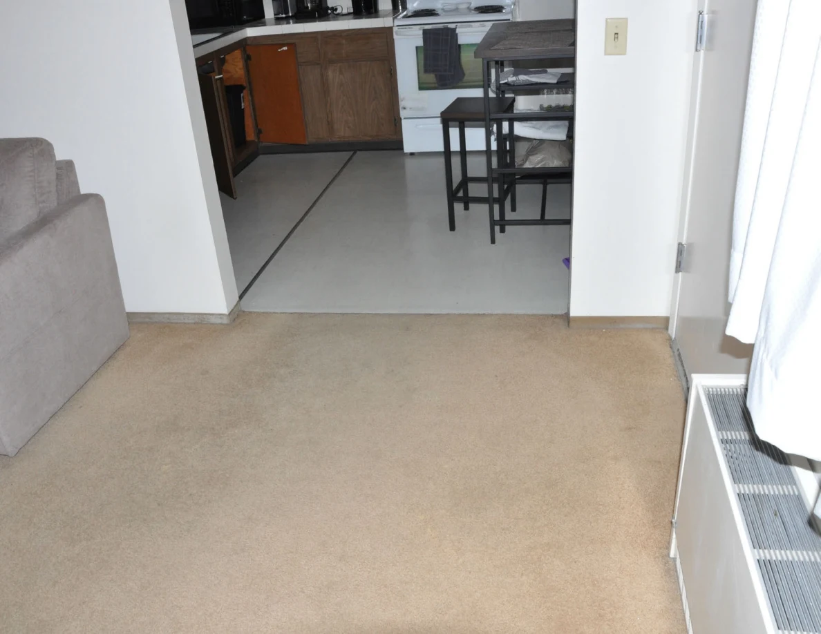 Beige carpet leading to a kitchen with a table, stools and white stove.