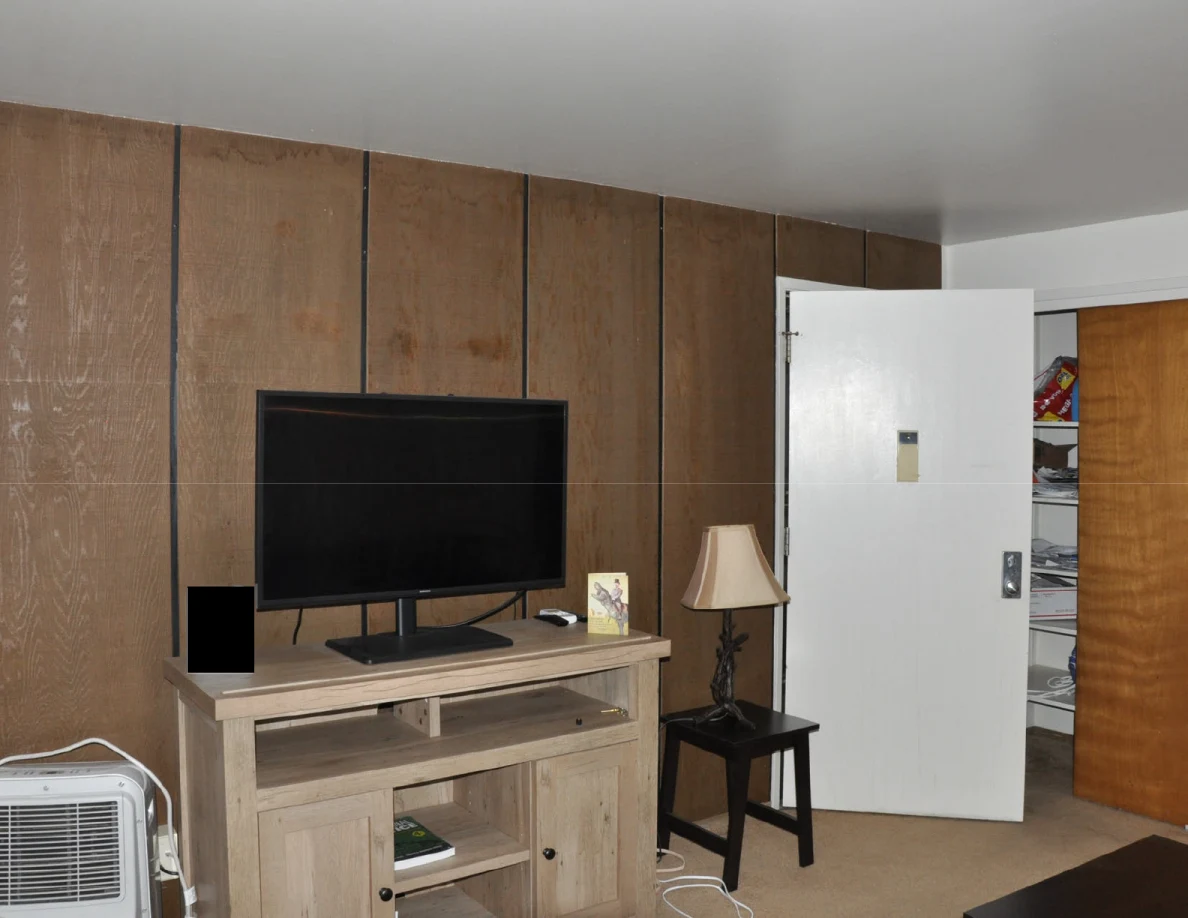 Television on a wooden cabinet beside a lamp and open white door; a small area is blacked out.