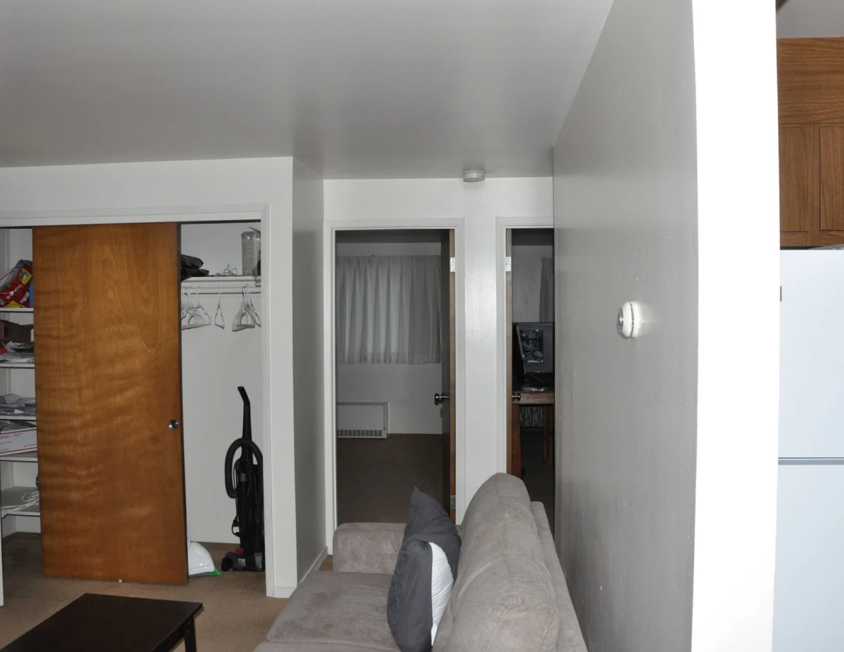 Side view of gray sofa and white wall beside an open closet and two interior doorways.