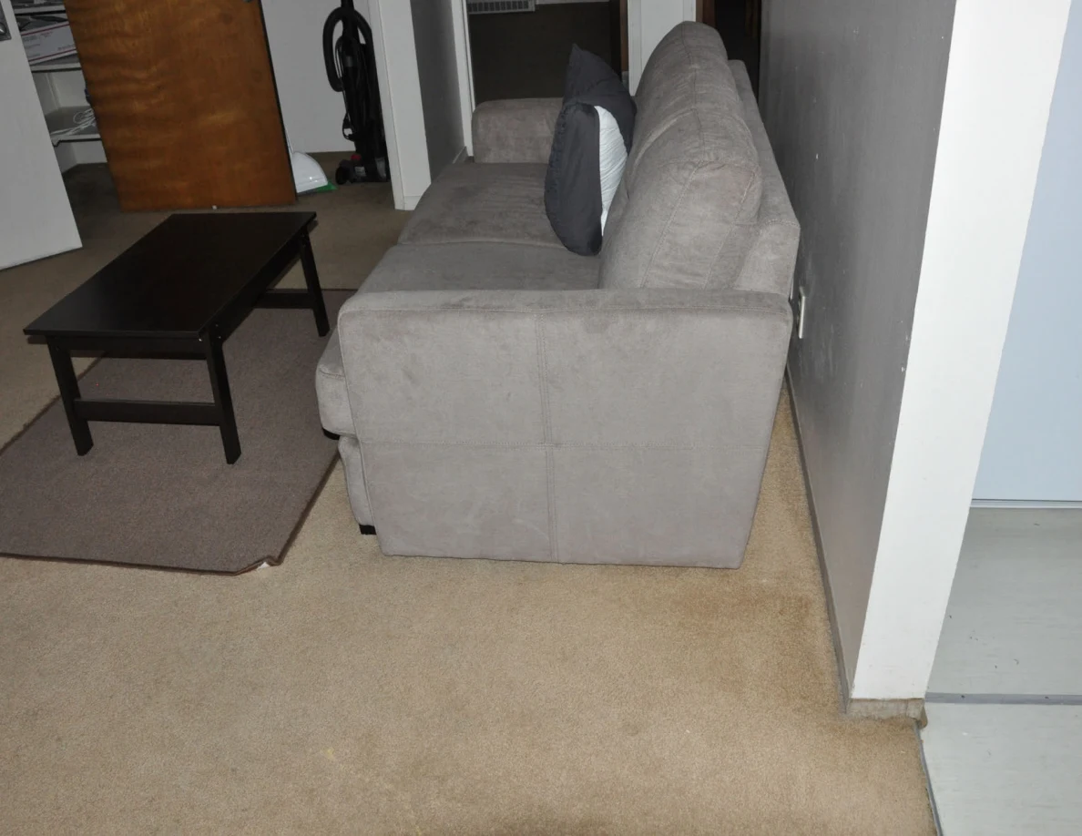 Side of a gray loveseat beside a coffee table on a rug and beige carpet.