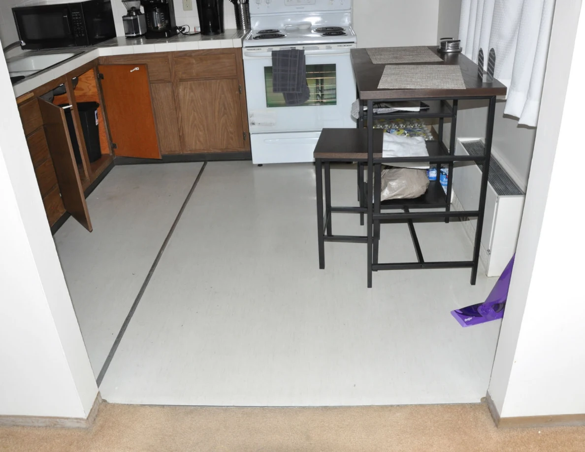 Kitchen floor with white stove, open sink cupboard, tall table, stools and purple mop.