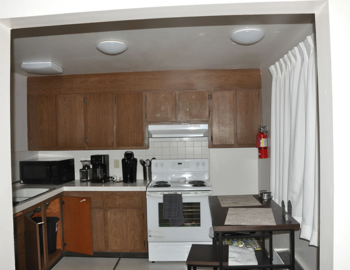 Kitchen with wooden cupboards, white stove, microwave, coffee makers and a small dining table.
