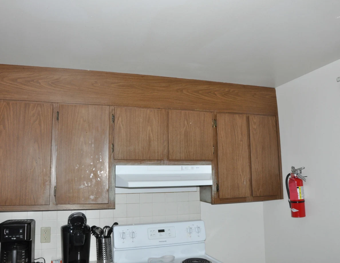 Wooden kitchen cabinets and range hood beside a red wall-mounted fire extinguisher.