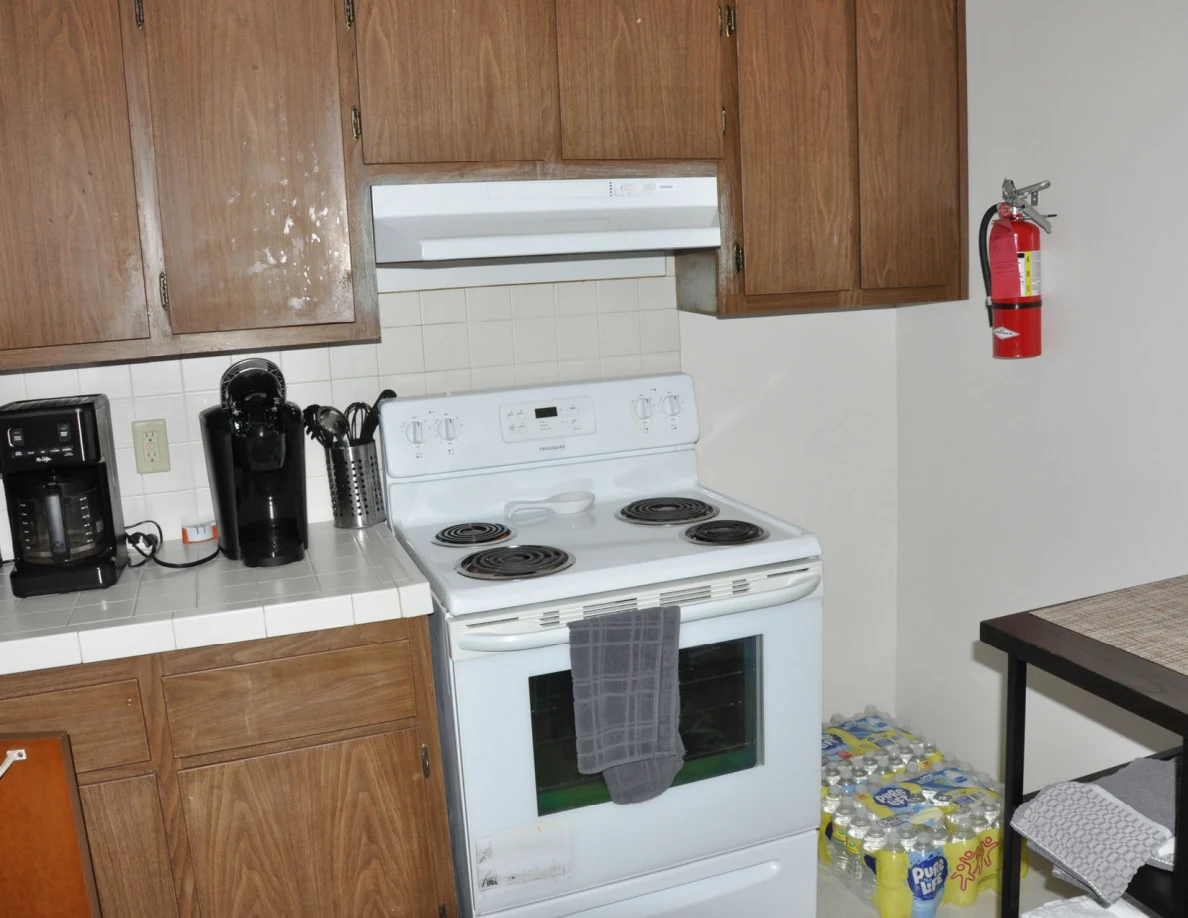 White electric stove with a towel on its oven handle, beside countertop appliances and a fire extinguisher.