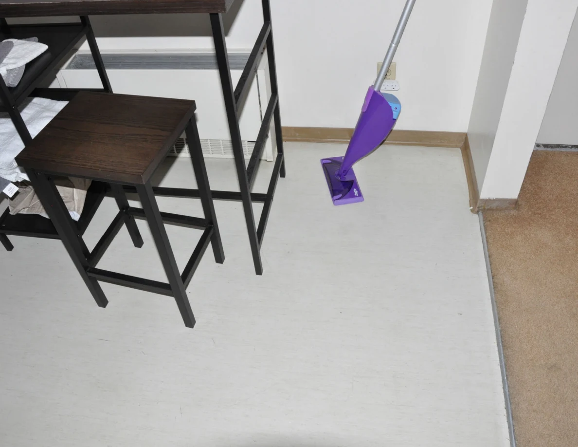Tall kitchen stool and purple spray mop on pale flooring.