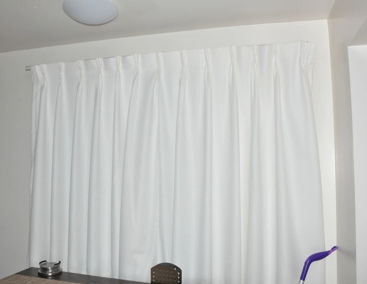 Closed white curtains above a dining table, with a round ceiling light.