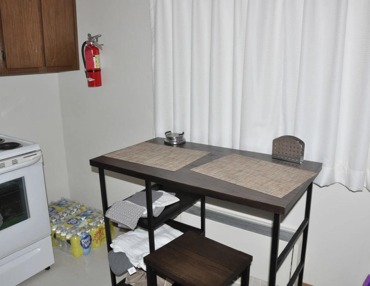 Dining table with placemats beneath curtains, beside a stove and fire extinguisher.