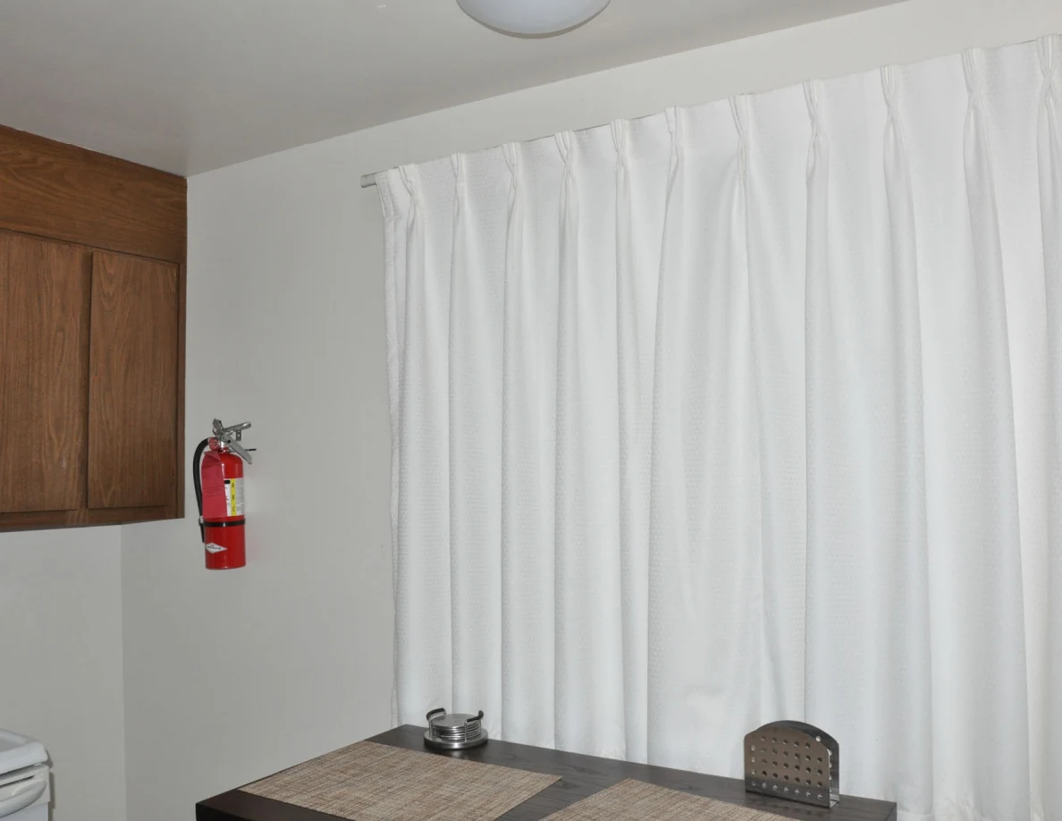 White curtains and red wall-mounted fire extinguisher above a dining table.