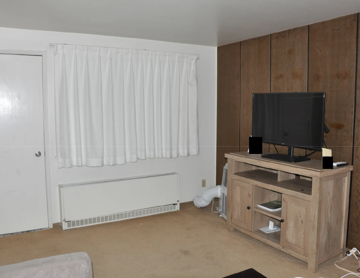 Living room with curtains, wall heater and television cabinet against wood paneling.