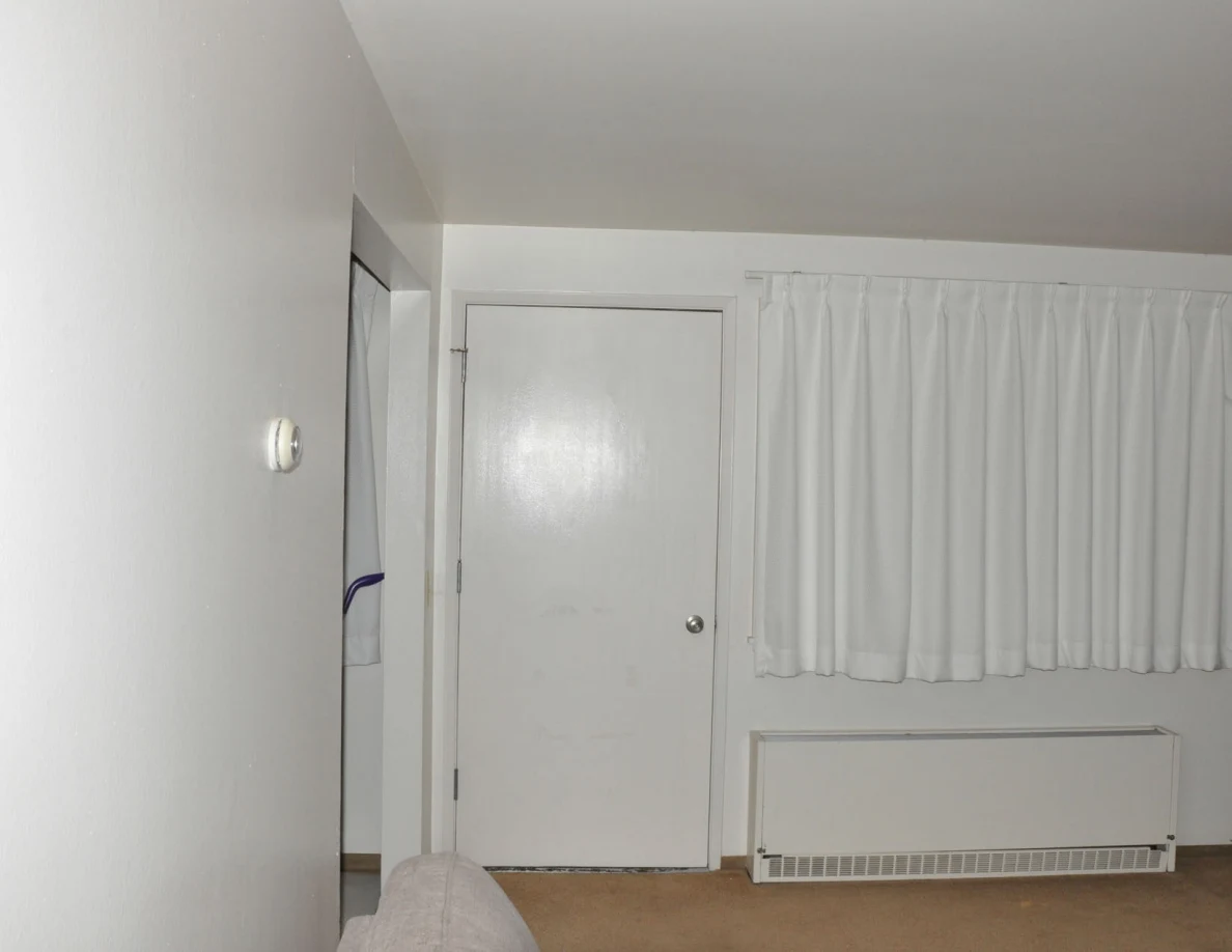 White door and curtains above a wall heater, seen from behind a sofa.