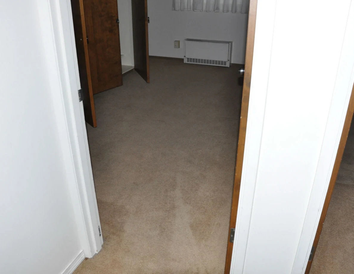 Beige carpet leading through a doorway into a room with a wall heater.