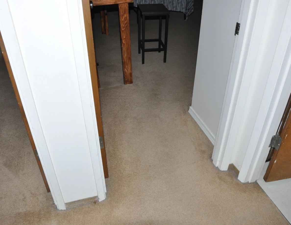 Carpeted doorway into a bedroom with a wooden desk and tall black stool.