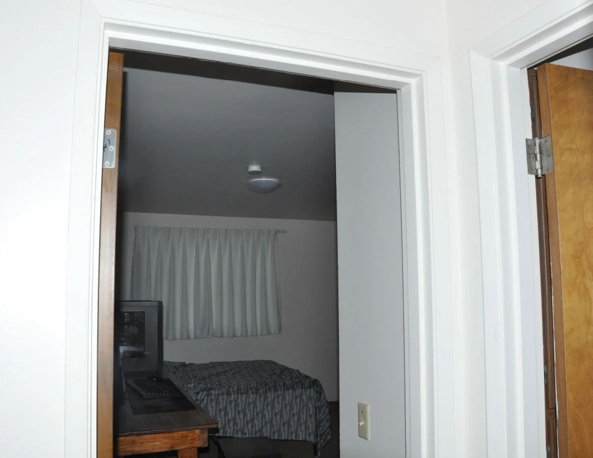 Upper bedroom doorway framing a bed, computer equipment, curtains and ceiling light.